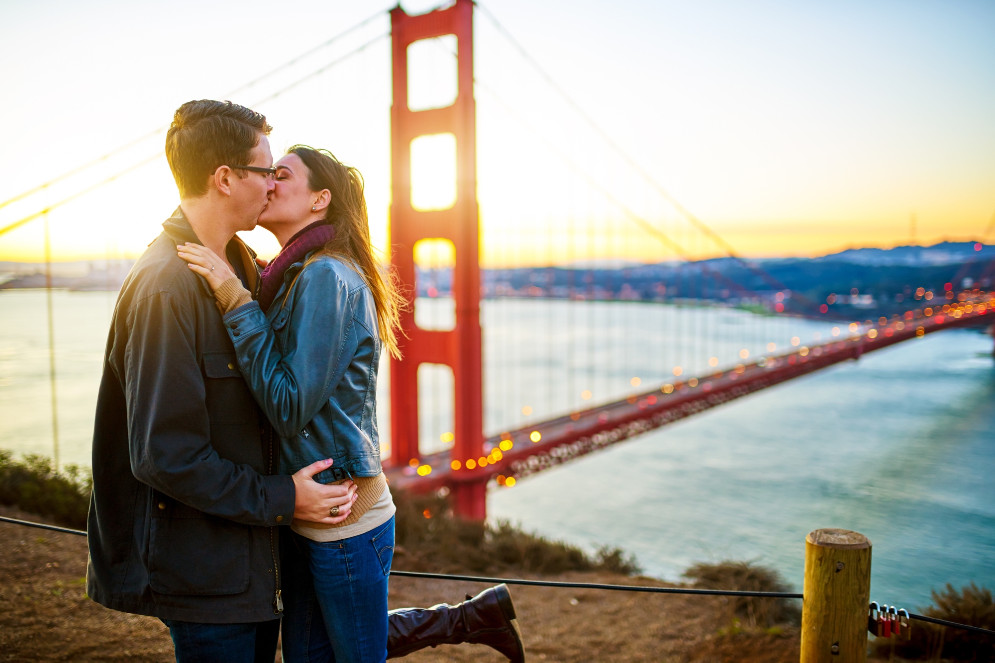 couple sharing a kiss in front of the golden gate bridge at sunrise