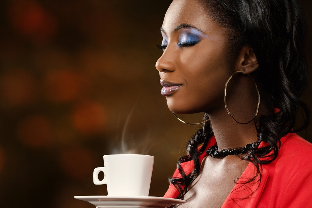 African woman smelling coffee with eyes closed.