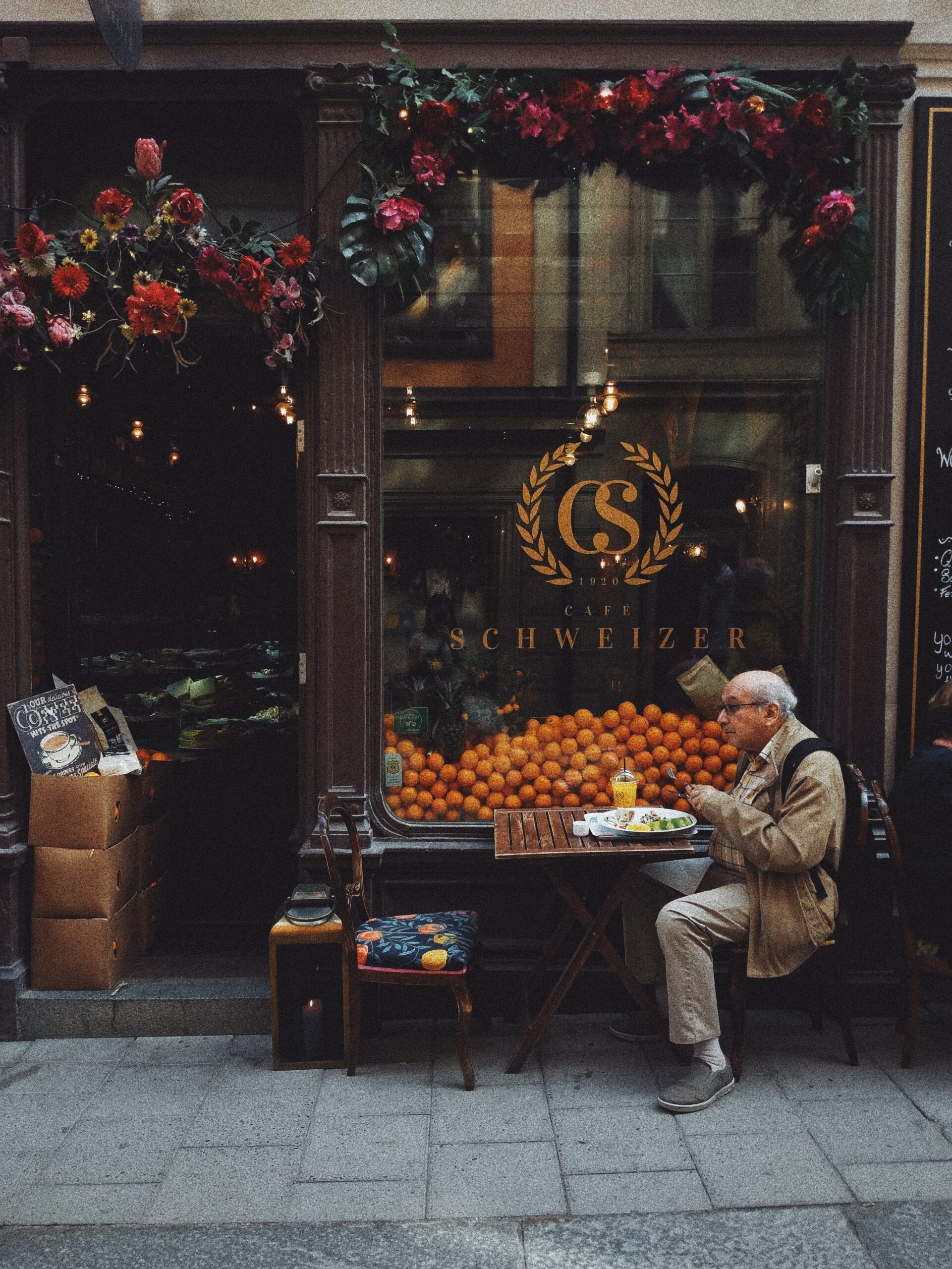 man-in-brown-jacket-sitting-on-chair-in-front-of-fruit-stand-3646171
